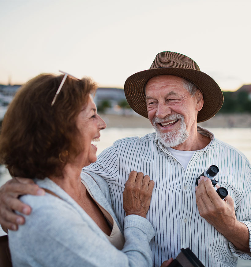 smiling senior couple with shore behind them